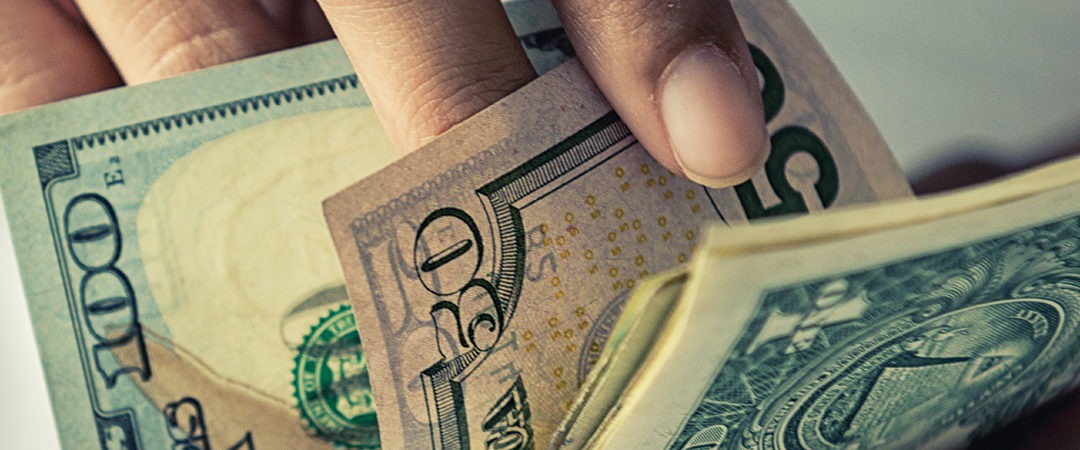 Close up view of a person thumbing through dollar bills.
